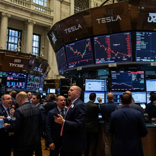 El parqué de la bolsa con pantallas que muestran gráficos de acciones de Tesla, mientras los especialistas discuten y realizan transacciones.